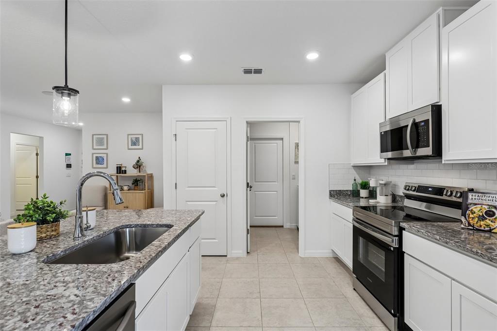 A kitchen with white cabinets, granite countertops, stainless steel appliances, and a central island sink — 5955 LYON ROAD, SPRING HILL, FL
