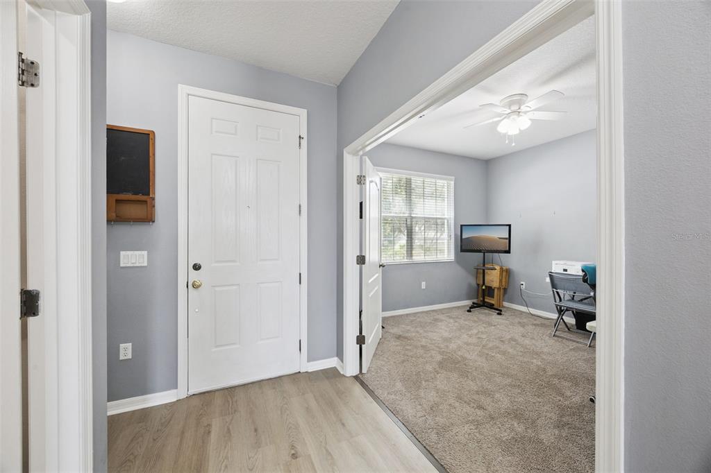 An entryway with light wood-look flooring leads into a carpeted room with a ceiling fan — 381 MISTY OAKS LANE, EUSTIS, FL