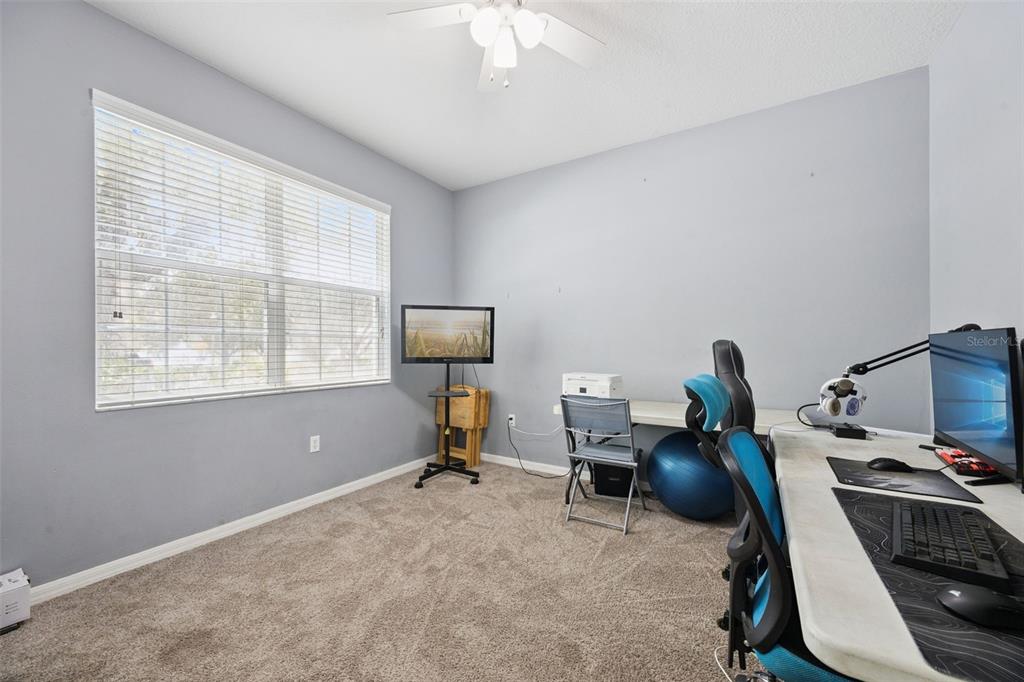 A home office with gray walls, carpeted flooring, a ceiling fan, and computer workstations — 381 MISTY OAKS LANE, EUSTIS, FL