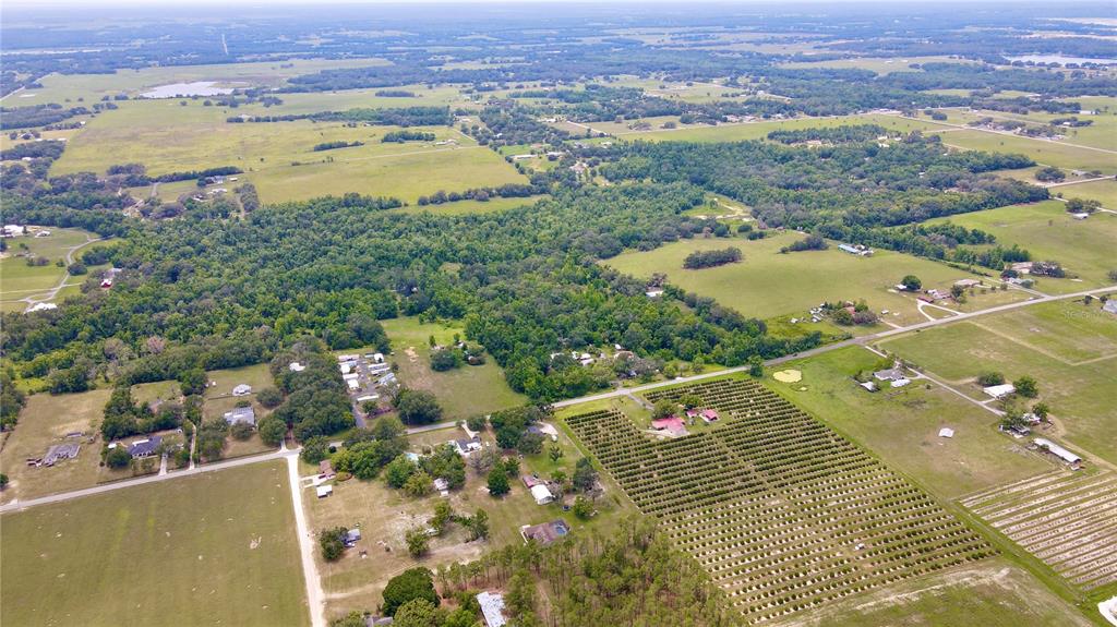 An aerial view shows a rural landscape with pastures, forested areas, and a large agricultural field — 14409 CURLEY ROAD, DADE CITY, FL