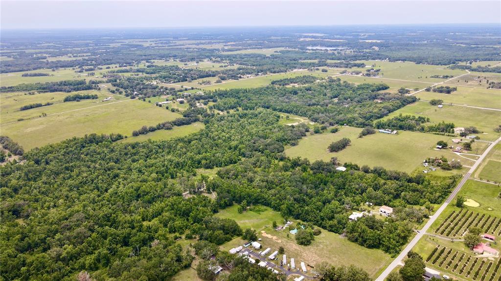 An aerial view shows a rural landscape with forested areas, open fields, and scattered houses — 14409 CURLEY ROAD, DADE CITY, FL