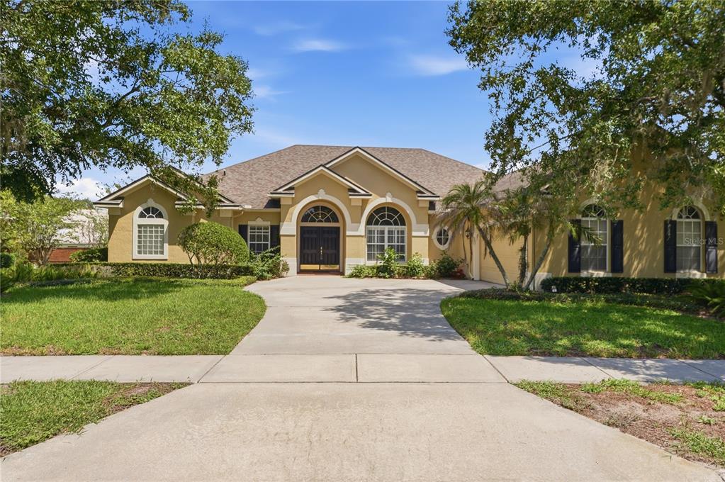 A single-story house with a tan stucco exterior, arched windows, and a concrete driveway — 11457 SWIFT WATER CIRCLE, ORLANDO, FL