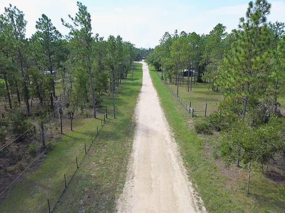 A long dirt driveway stretches through a wooded lot with wire fencing on both sides — TBD NE 93RD TERRACE, ARCHER, FL