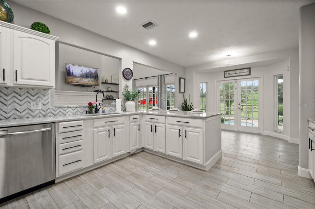 A bright kitchen features white cabinets, a chevron backsplash, stainless steel appliances, and tile flooring — 2393 APPY LANE, APOPKA, FL