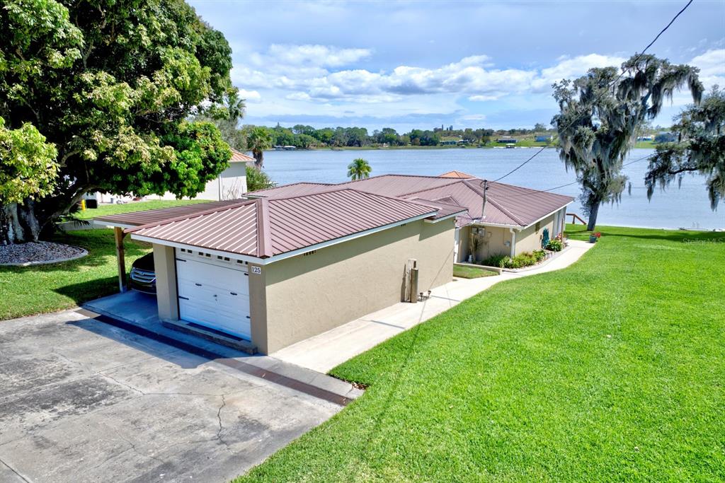 An aerial view of a tan house with a metal roof and garage by a lake — 125 MCCOY DRIVE, LAKE PLACID, FL