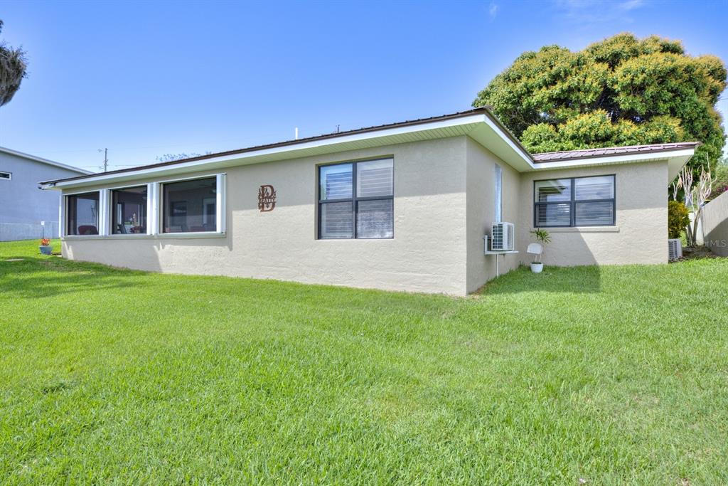 The exterior of a single-story house with a tan stucco finish and a grassy yard — 125 MCCOY DRIVE, LAKE PLACID, FL