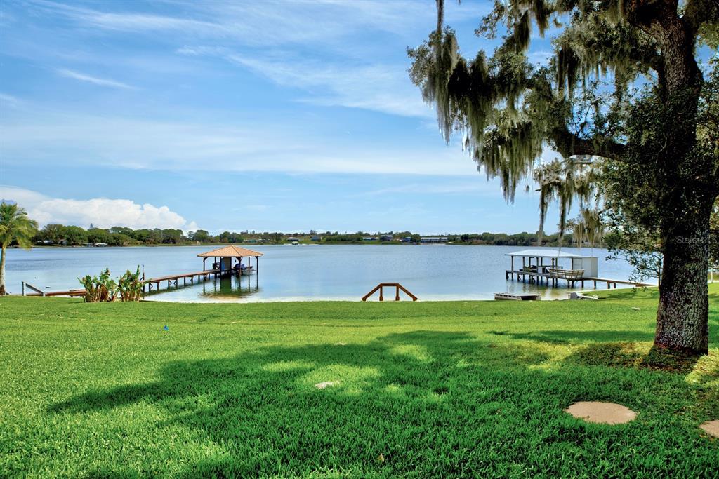 A grassy lawn leads to a lake with two wooden docks under a blue sky — 125 MCCOY DRIVE, LAKE PLACID, FL
