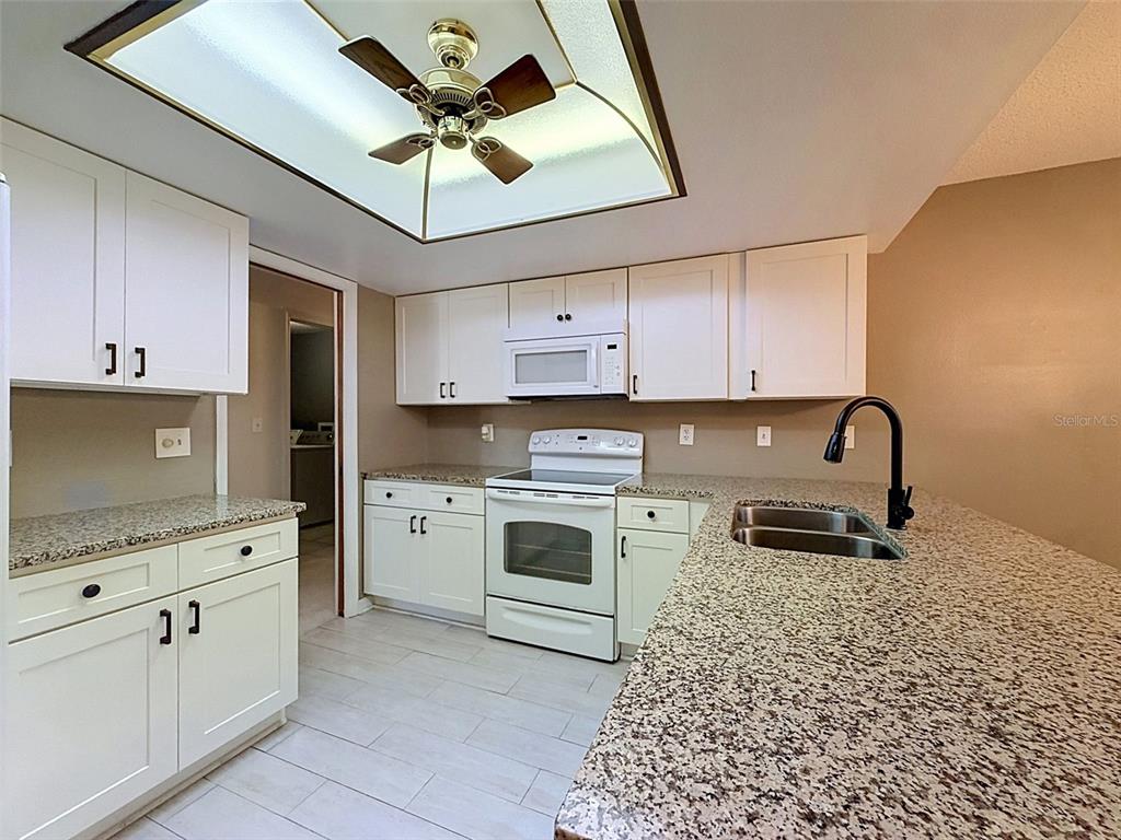 A kitchen features white cabinets, granite countertops, a white stove, and a ceiling fan — 7308 BALTUSROL DRIVE, NEW PORT RICHEY, FL