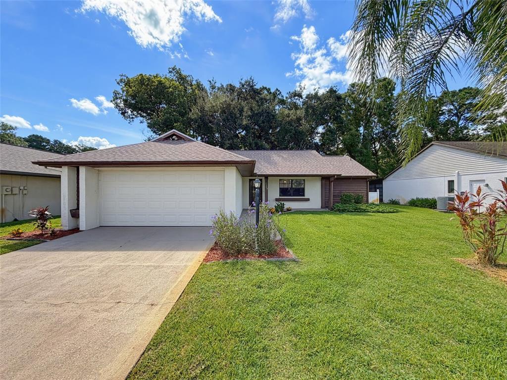 A single-story house with a white garage door, a concrete driveway, and a grassy lawn — 7308 BALTUSROL DRIVE, NEW PORT RICHEY, FL