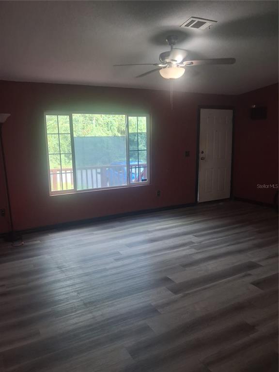 A living room with dark red walls, wood-look flooring, a ceiling fan, and a large window — 8500 NW 10TH TERRACE, OCALA, FL