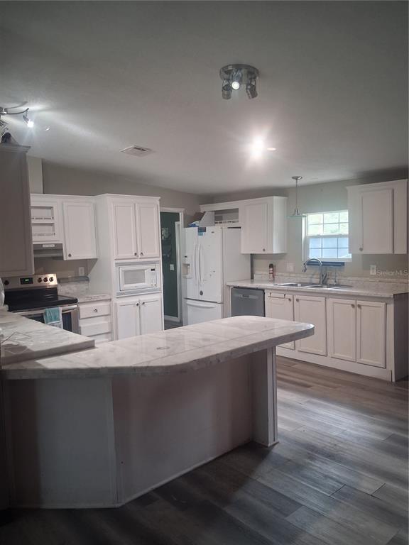 A kitchen features white cabinets, a peninsula, stainless steel appliances, and wood-look flooring — 8500 NW 10TH TERRACE, OCALA, FL