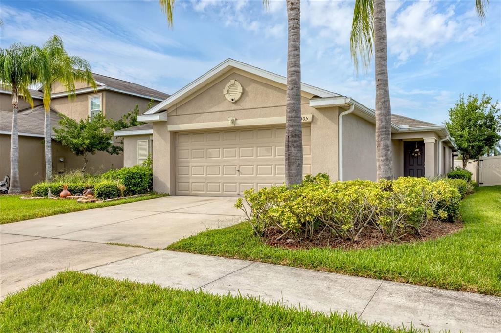 A tan single-story house with a two-car garage, palm trees, and a landscaped front yard — 16505 MYRTLE SAND DRIVE, WIMAUMA, FL