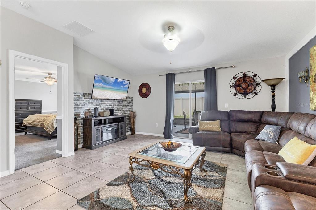 A living room features a brown sectional sofa, a glass coffee table, and a brick-accented wall — 16505 MYRTLE SAND DRIVE, WIMAUMA, FL