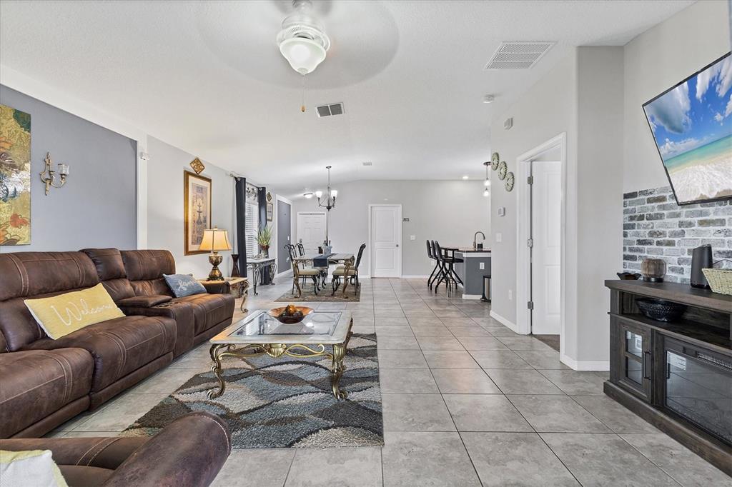 An open-concept living and dining area features tile flooring, a brown leather sofa, and kitchen — 16505 MYRTLE SAND DRIVE, WIMAUMA, FL