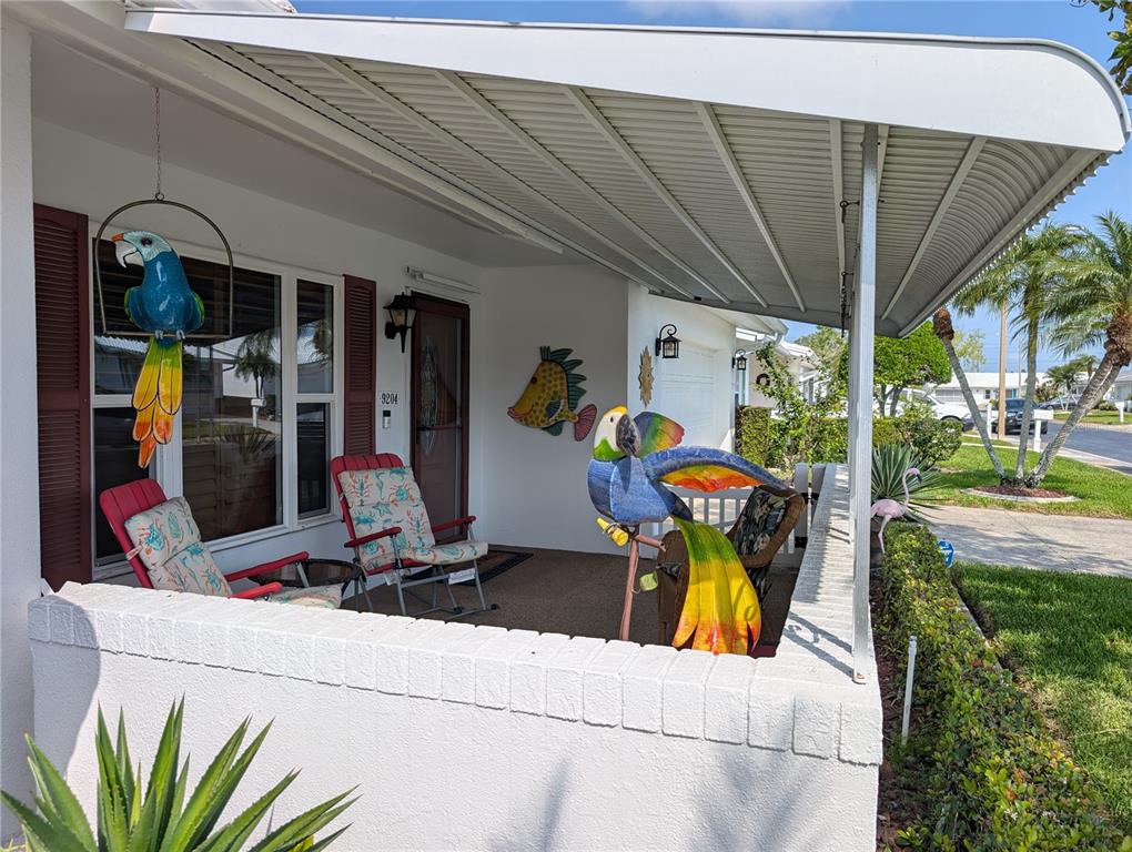 A covered front porch features white brick walls, outdoor chairs, and colorful parrot and fish decor — 9204 36TH WAY N UNIT 6, PINELLAS PARK, FL