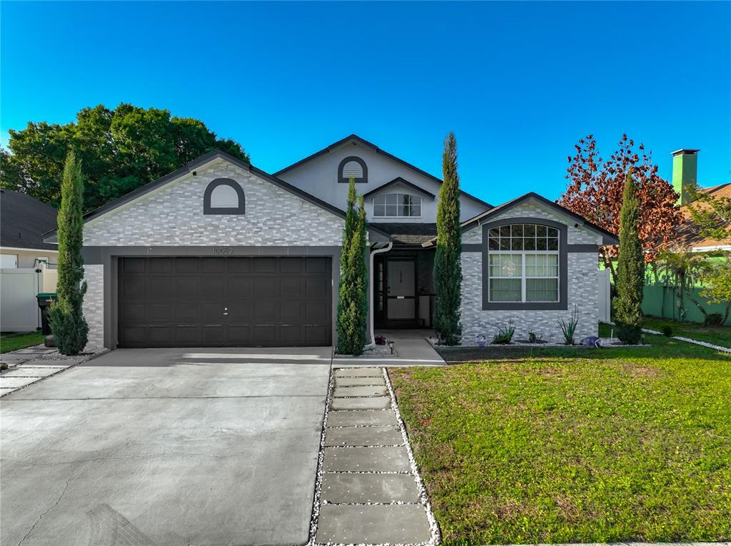 A single-story house with a gray stone facade, a two-car garage, and tall cypress trees — 10052 SANDBAR STREET, ORLANDO, FL