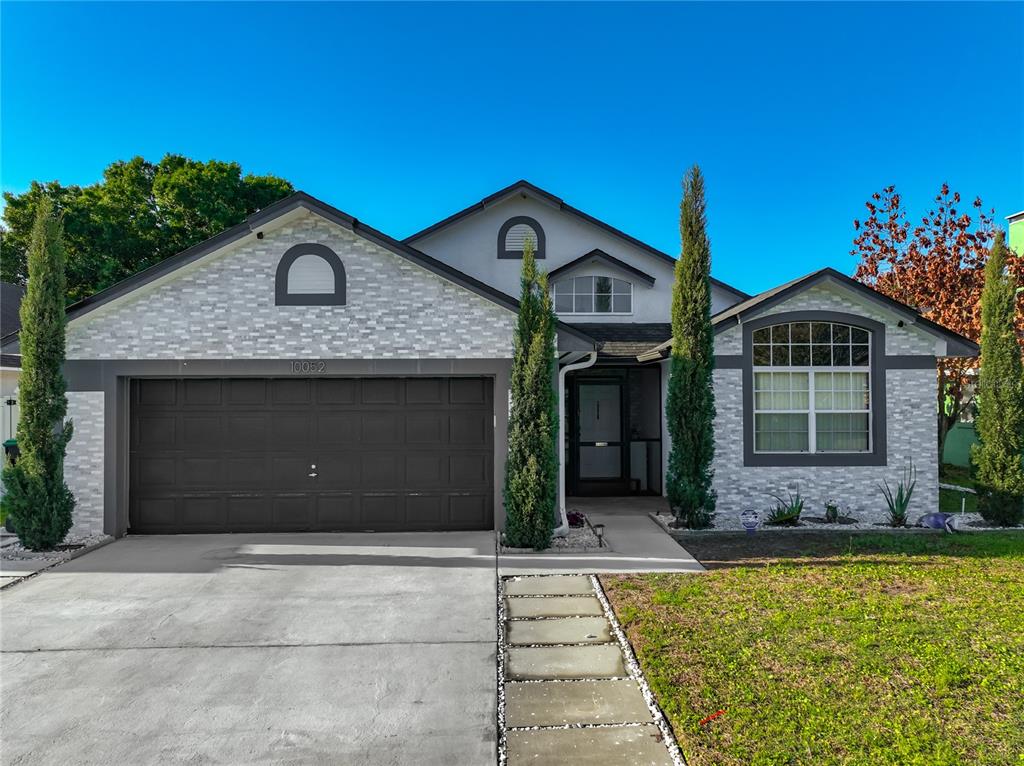 A single-story house with a gray stone facade, a two-car garage, and three tall cypress trees — 10052 SANDBAR STREET, ORLANDO, FL