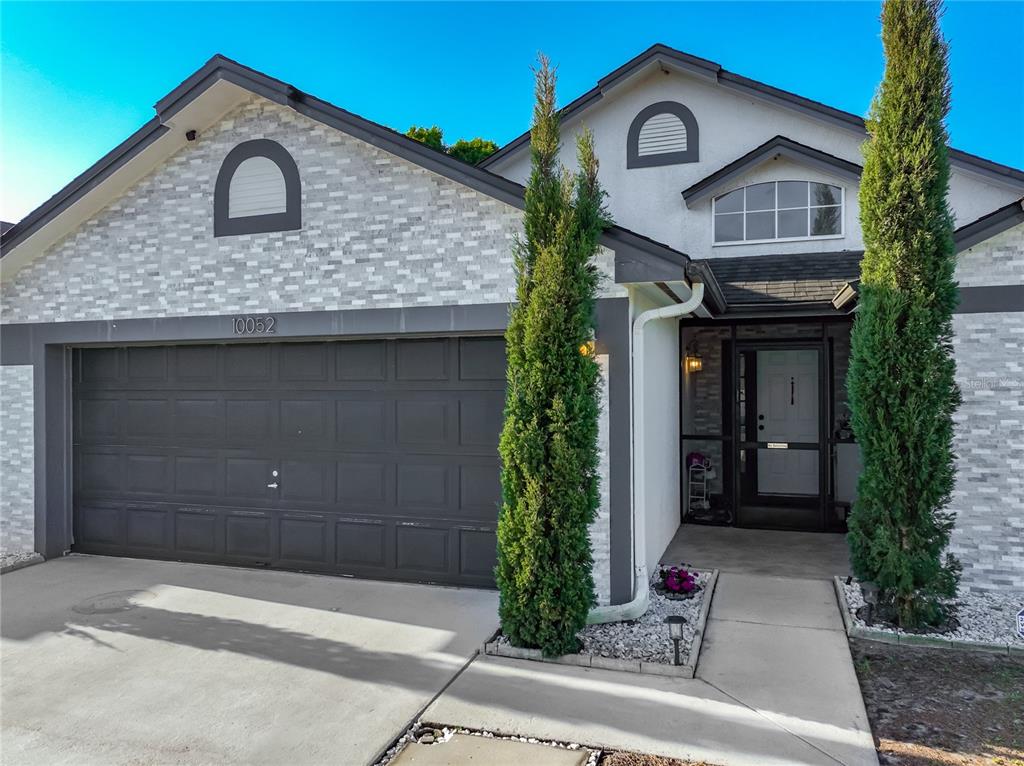 A single-story house with a gray garage, stone veneer siding, and two tall, thin evergreen trees — 10052 SANDBAR STREET, ORLANDO, FL