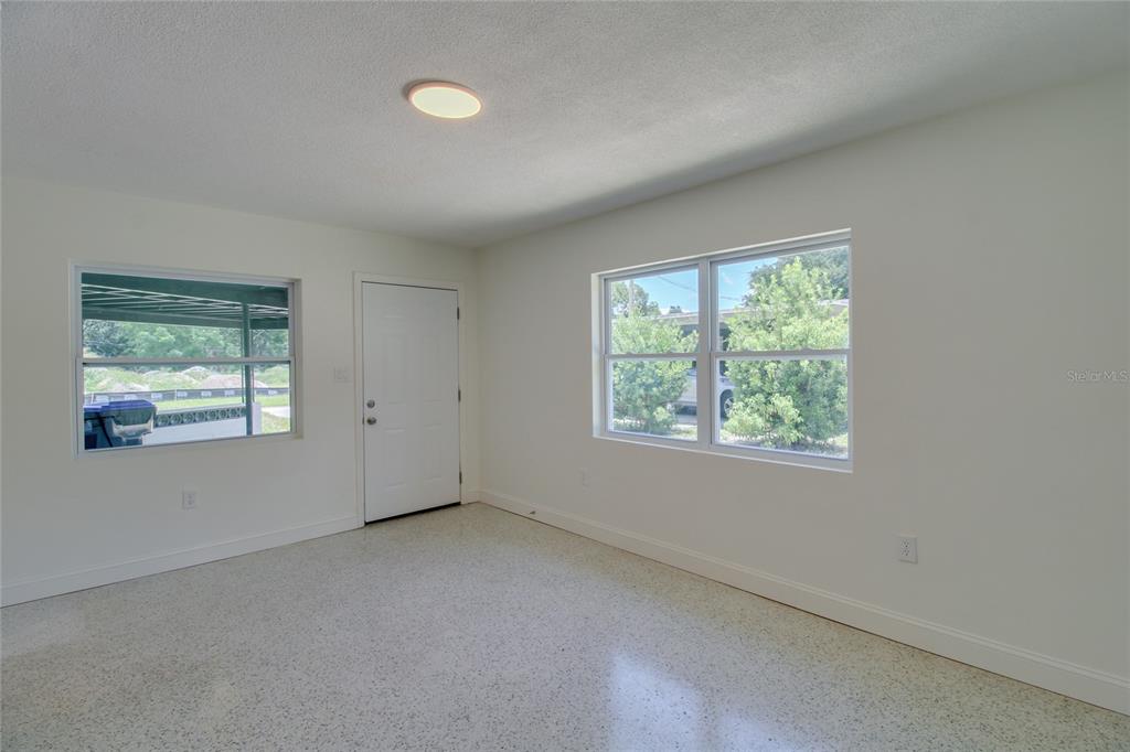 An empty room features white walls, a light-colored terrazzo floor, two windows, and a door — 1618 INDIANA AVENUE, WINTER PARK, FL