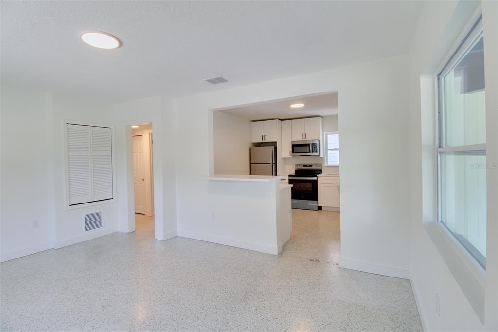 A bright room with white walls, terrazzo flooring, and an open kitchen with white cabinets — 1618 INDIANA AVENUE, WINTER PARK, FL