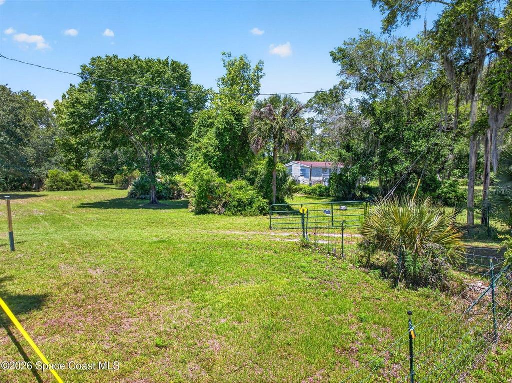 A grassy, fenced lot features mature trees and a small house in the background — 6700 US HIGHWAY 1, MIMS, FL