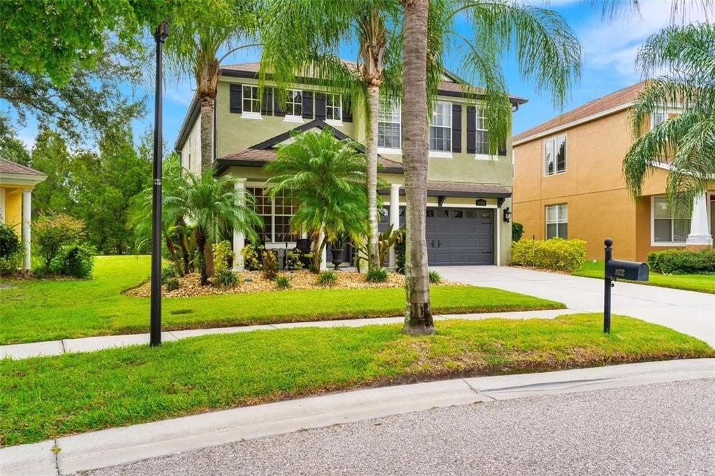 A two-story green house with a front porch, palm trees, and a two-car garage — 1122 NASHVILLE DRIVE, WESLEY CHAPEL, FL