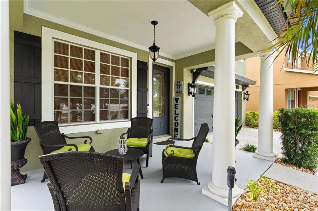 A covered front porch features wicker chairs with lime green cushions and a small table — 1122 NASHVILLE DRIVE, WESLEY CHAPEL, FL