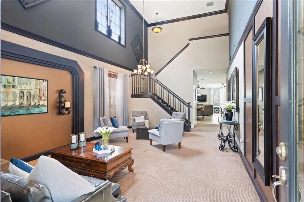 A two-story foyer features a staircase, dark wood trim, and a seating area with armchairs — 1122 NASHVILLE DRIVE, WESLEY CHAPEL, FL