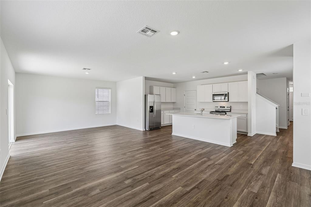 An open-concept living area with wood-look flooring, a white kitchen island, and stainless steel appliances — 5373 WILLOW CREEK, HAINES CITY, FL