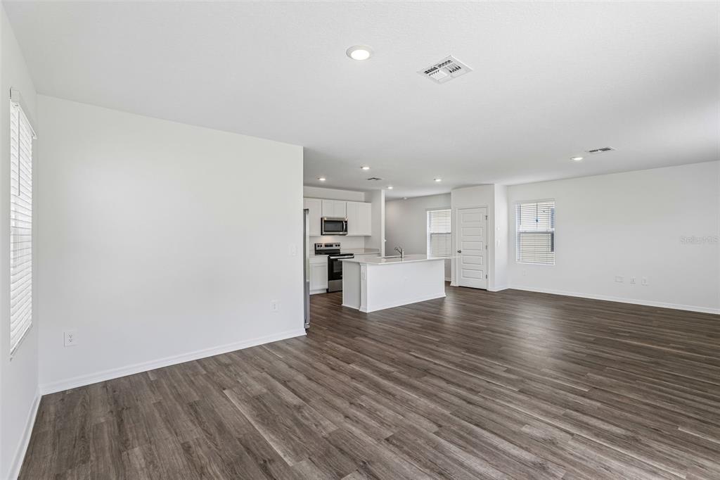 An open-concept living area features wood-look flooring, white walls, and a kitchen with white cabinetry — 5373 WILLOW CREEK, HAINES CITY, FL