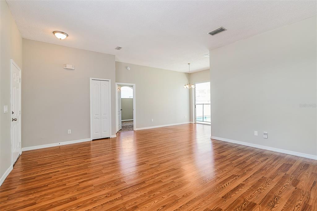 An empty living room with light-colored walls, wood-look flooring, a closet, and a sliding glass door — 8615 CAVENDISH DRIVE, KISSIMMEE, FL