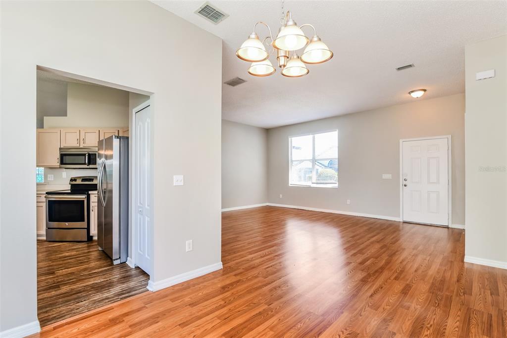 A living room with wood-look flooring and a chandelier opens into a kitchen with appliances — 8615 CAVENDISH DRIVE, KISSIMMEE, FL