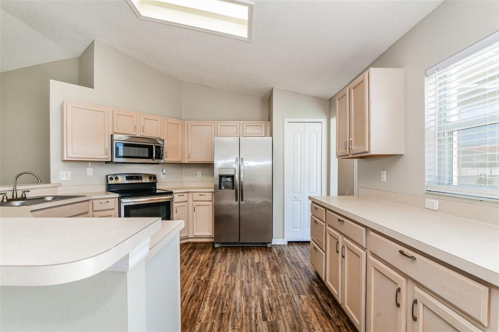A kitchen features light-colored cabinets, stainless steel appliances, and wood-look flooring under a vaulted ceiling — 8615 CAVENDISH DRIVE, KISSIMMEE, FL
