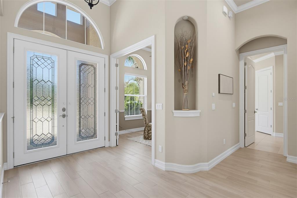 A bright entryway features light wood-look tile flooring, a double glass-paneled front door, and an arched wall niche — 206 WILLOW OAK WAY, PALM COAST, FL