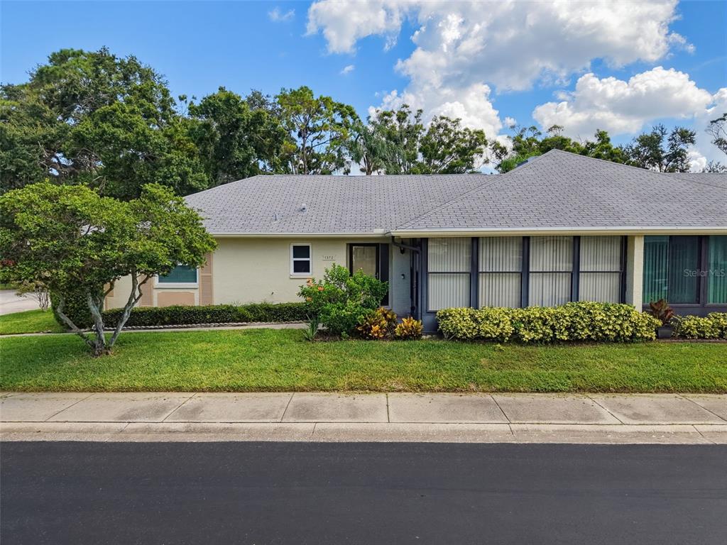 A single-story house with a gray shingled roof, light-colored siding, and a front lawn — 1372 CARLISLE COURT, DUNEDIN, FL