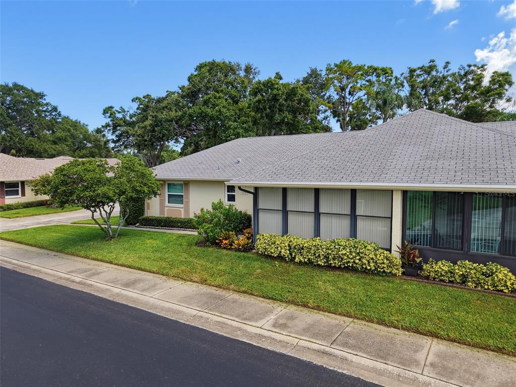 A single-story house with a gray shingled roof, a screened-in porch, and a grassy lawn — 1372 CARLISLE COURT, DUNEDIN, FL