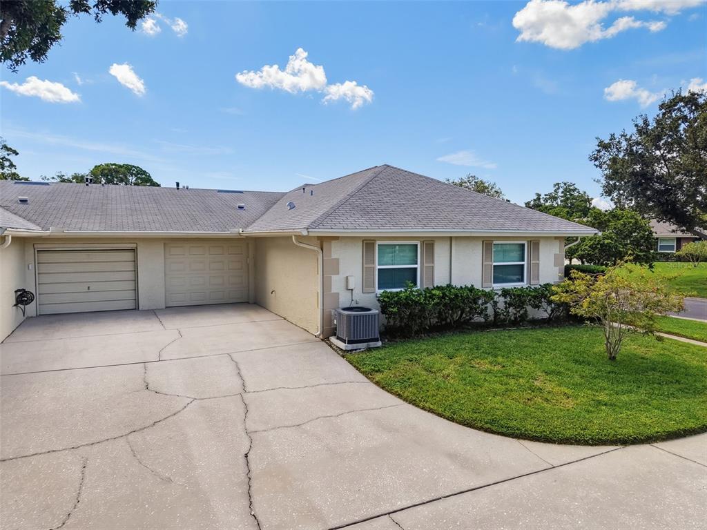 A single-story house exterior features a beige stucco facade, a gray shingled roof, and a driveway — 1372 CARLISLE COURT, DUNEDIN, FL