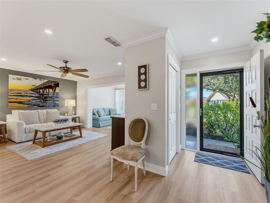 A bright entryway leads into a living room with light wood floors and a sofa — 1372 CARLISLE COURT, DUNEDIN, FL