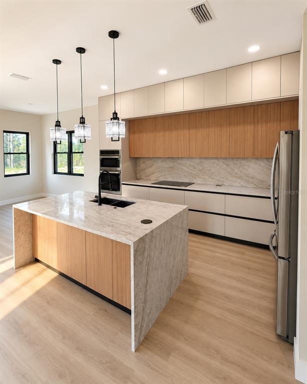 A modern kitchen features a marble waterfall island, wood-toned cabinetry, and stainless steel appliances — 19215 NUTMEG ST, ORLANDO, FL