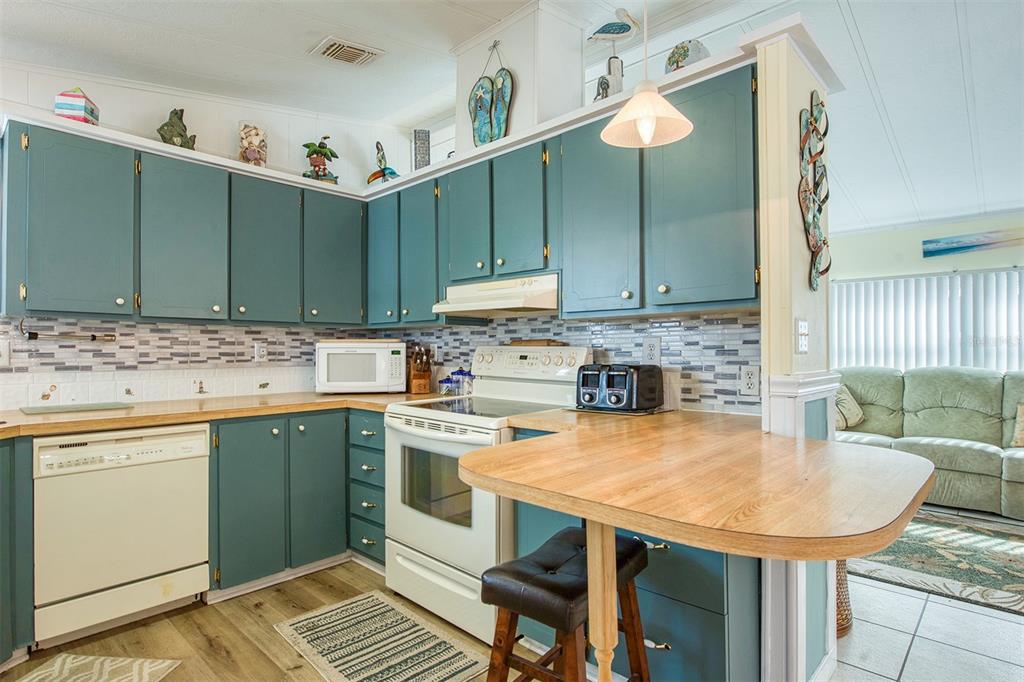 A kitchen with teal cabinets, wood countertops, a white stove, and a breakfast bar — 83 PELICAN DRIVE N, OLDSMAR, FL