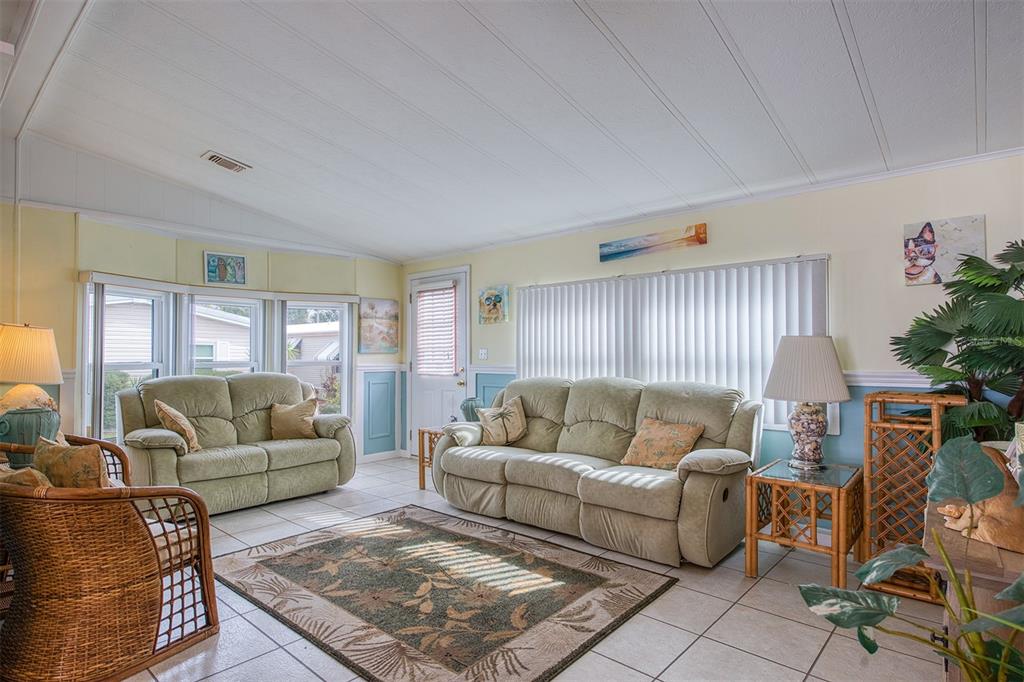 A living room features light-colored tile floors, two sofas, a wicker chair, and vertical blinds — 83 PELICAN DRIVE N, OLDSMAR, FL