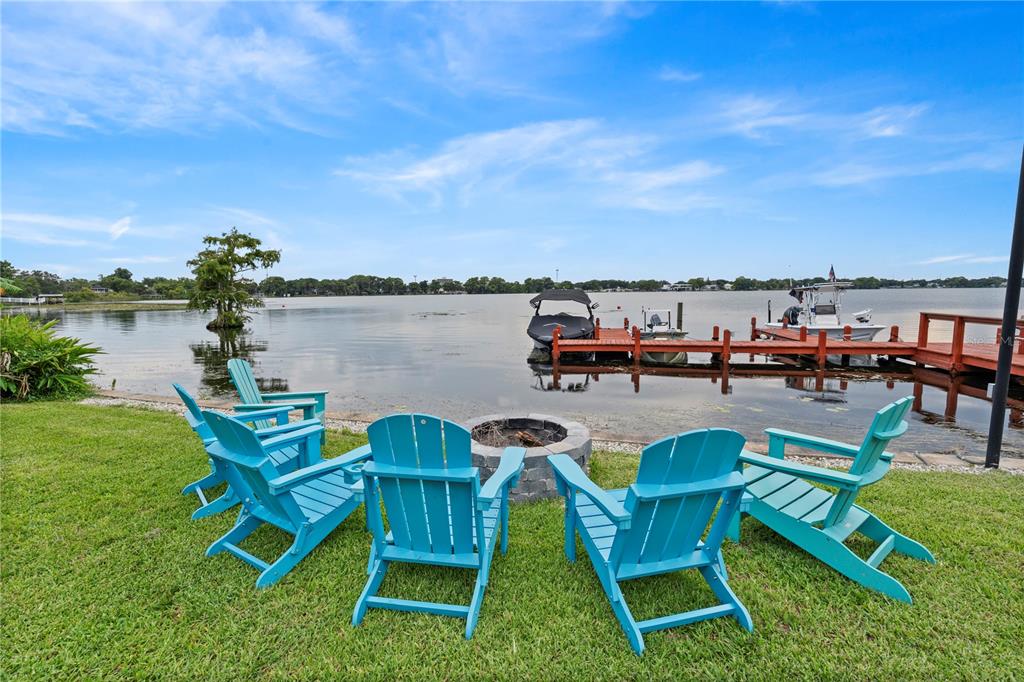 Four bright blue Adirondack chairs surround a stone fire pit overlooking a lake and dock — 151 N ORLANDO AVENUE UNIT 261, WINTER PARK, FL
