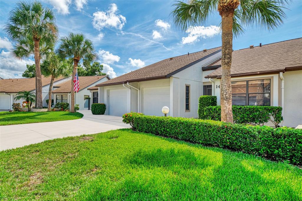 A single-story residential building with a two-car garage, manicured hedges, and palm trees — 1211 CAPRI ISLES BOULEVARD UNIT 14, VENICE, FL