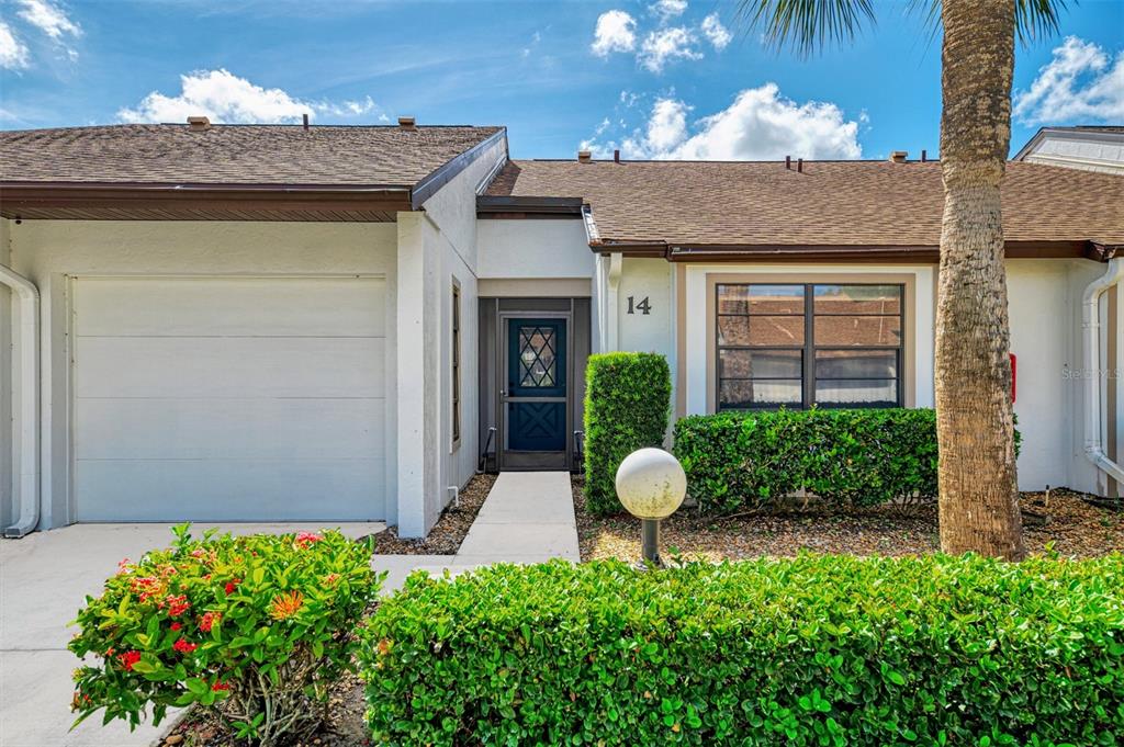 The exterior of a single-story home features a garage, a front entrance, and landscaped hedges — 1211 CAPRI ISLES BOULEVARD UNIT 14, VENICE, FL