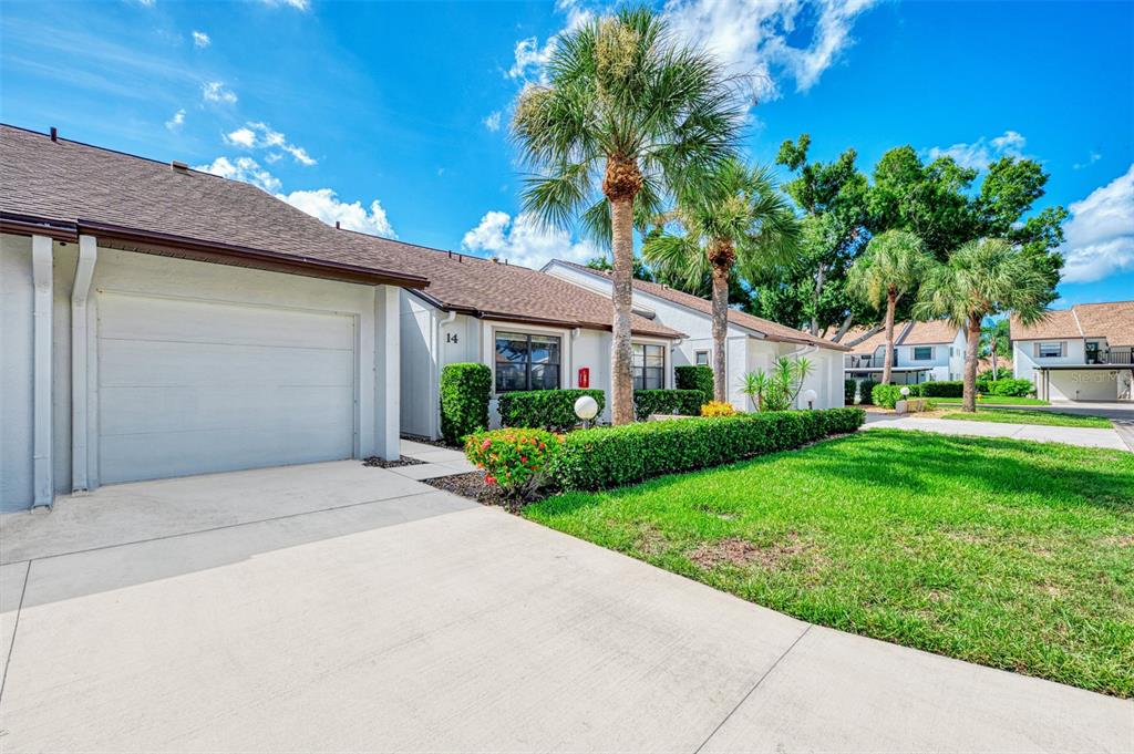 A single-story residential building with a garage, a concrete driveway, and manicured landscaping — 1211 CAPRI ISLES BOULEVARD UNIT 14, VENICE, FL