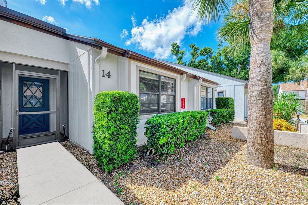 The exterior of a single-story residential unit features a blue screen door and number 14 — 1211 CAPRI ISLES BOULEVARD UNIT 14, VENICE, FL