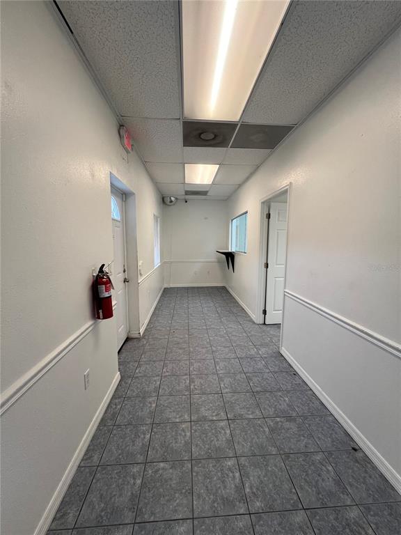 A narrow hallway with gray tiled flooring, white walls, and a drop ceiling with lights — 7216 CHANCERY UNIT 100, ORLANDO, FL