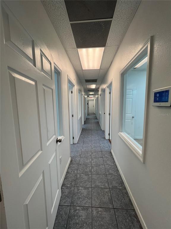 A long, narrow office hallway features gray tiled flooring, white doors, and a drop ceiling — 7216 CHANCERY UNIT 100, ORLANDO, FL