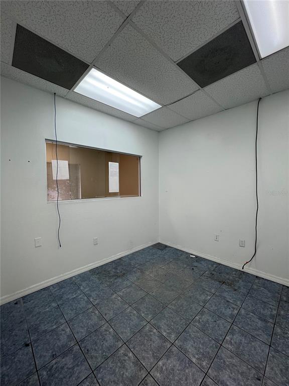 An empty office room features blue tiled flooring, white walls, and a drop ceiling — 7216 CHANCERY UNIT 100, ORLANDO, FL