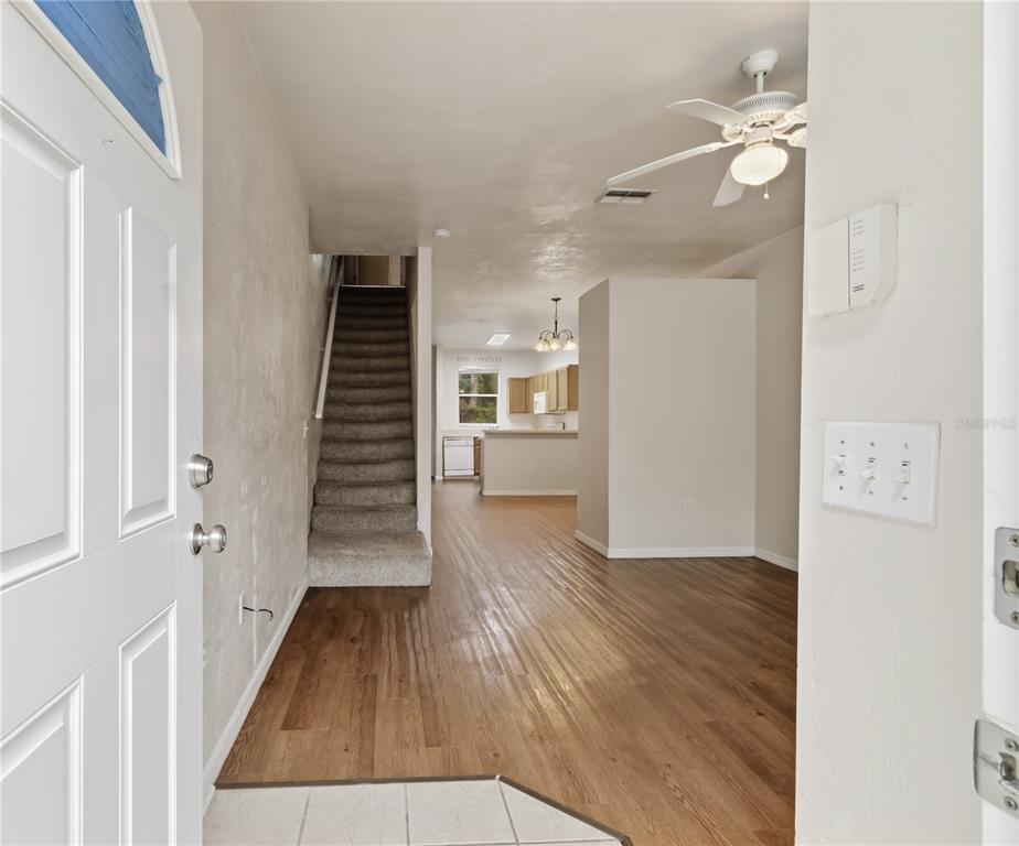 An entryway leads to a carpeted staircase, wood-look flooring, and an open kitchen beyond — 4415 SW 34TH STREET UNIT 309, GAINESVILLE, FL